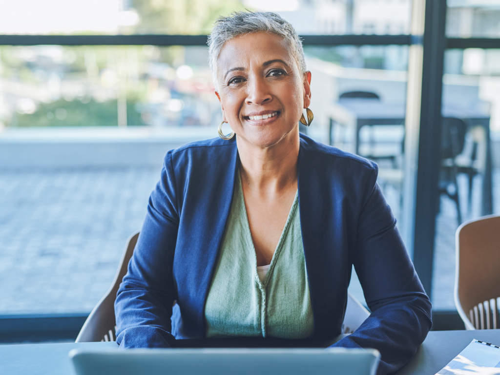 Mature executive with a laptop smiling, looking happy and waiting or listening to a job candidate at an interview. Portrait of a friendly human resource manager ready to meet employee in a restaurant Führungskräftecoaching